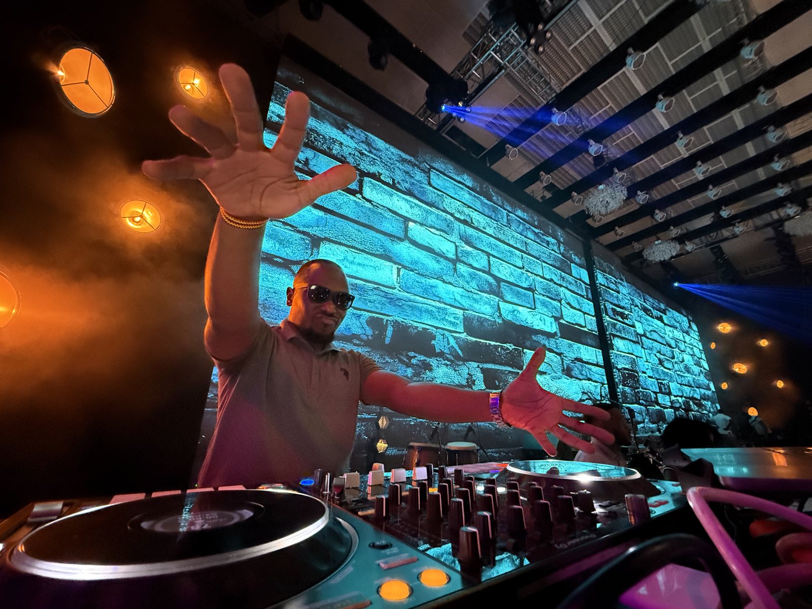 Moustey at the decks, arms out to the crowd under blue stage lights