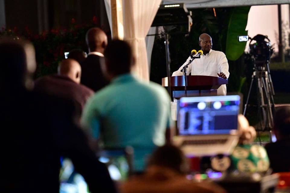 A speaker at the podium, seen past the DJ setup at an evening corporate event